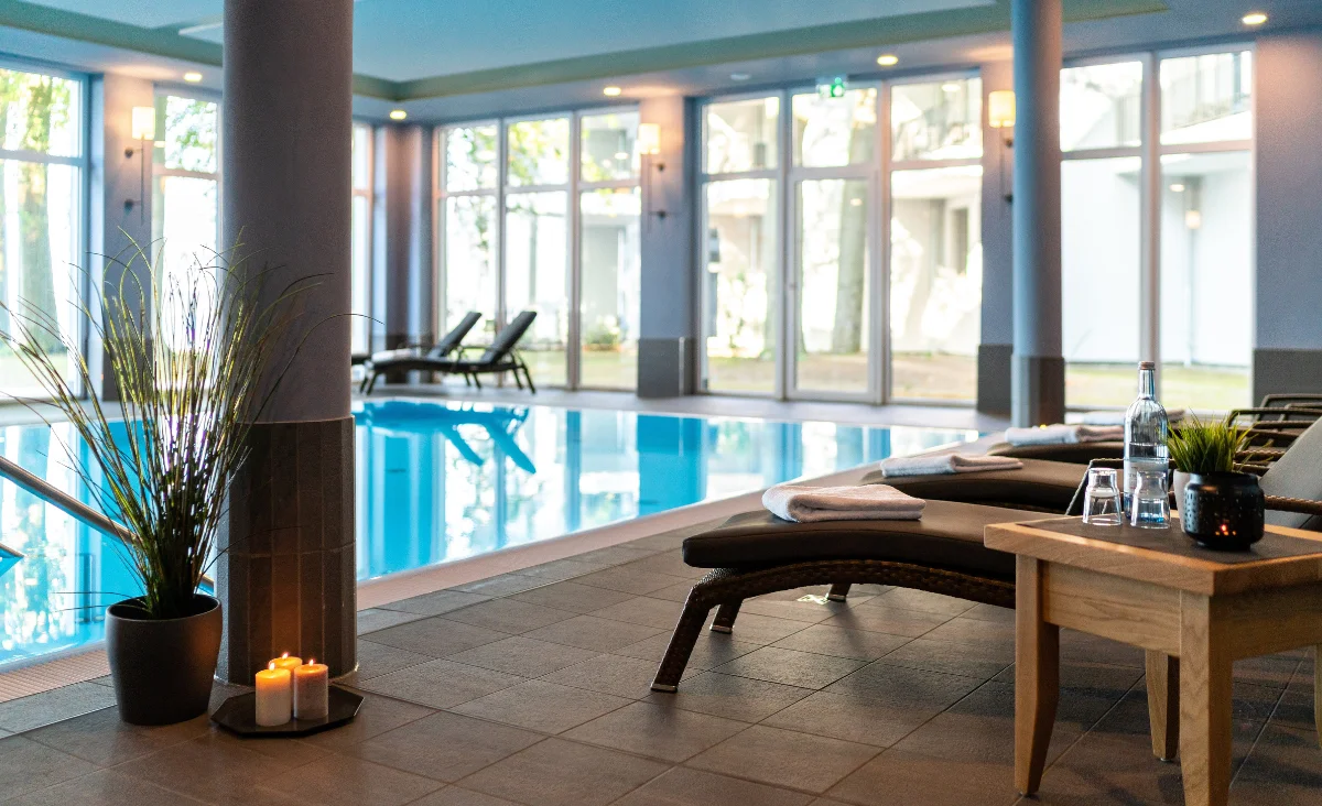Innenansicht des Schwimmbads im Aparthotel Müritzpalais mit Liegen, Tisch, Pflanzen und Kerzen